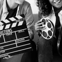 Dwie osoby z klapsem filmowym i rolką taśmy filmowej. Zastanawiasz się, ile zarabia producent filmowy?