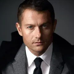 James Badge Dale w szarym garniturze i czarnym krawacie, z niebieskimi oczami wpatrującymi się w obiektyw.