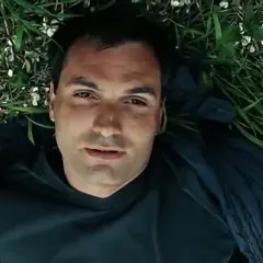 Mężczyzna leży na trawie, otoczony zielenią i białymi kwiatkami. Może to scena z filmu, gdzie wino truskawkowe obsada odgrywa ważną rolę.