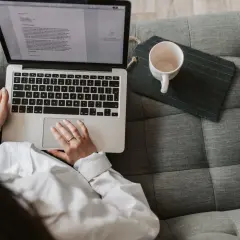 Kobieta pisze na laptopie, zastanawiając się, ile zarabia scenarzysta w Polsce. Obok kubek i tablet.