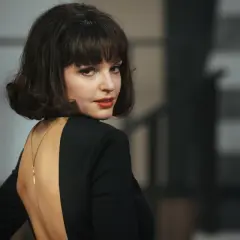 Elegancka Maria Dębska w czarnej sukni z głębokim wycięciem na plecach, zmysłowo odwraca głowę.