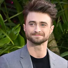 Daniel Radcliffe, który grał Harry'ego Pottera, w szarym garniturze na tle zieleni.