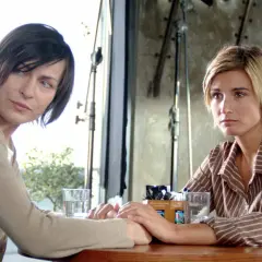 Dwie kobiety trzymają się za ręce przy stoliku. W tle widać sprzęt filmowy. To scena z filmu "Nigdy w życiu".