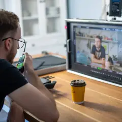 Producenci na planie filmowym czuwają nad realizacją, jeden z nich rozmawia przez krótkofalówkę, monitorując obraz na ekranie.
