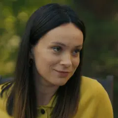 Uśmiechnięta Maria Dejmek w żółtym swetrze, z rozpuszczonymi włosami, na tle zieleni.
