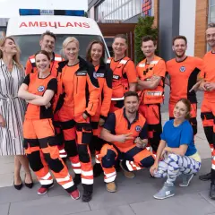 Ekipa ratowników medycznych w pomarańczowych strojach, którzy grają w serialu "Na sygnale", pozuje przed karetką.
