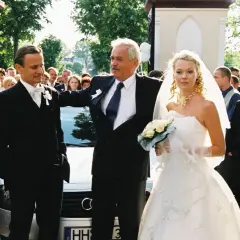 Para młoda i goście na weselu Smarzowskim. Panna młoda w białej sukni, pan młody w garniturze.