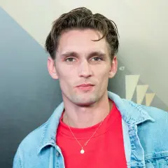 Filip Gurłacz, aktor, w czerwonej bluzie i jeansowej kurtce, z naszyjnikiem.