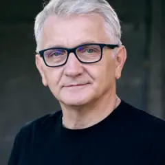 Portret Dariusza Kowalskiego, aktora, w okularach i czarnej koszulce.