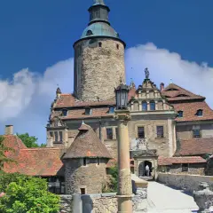 Zamek Czocha z wieżą i kamiennym mostem, pod błękitnym niebem z chmurami.