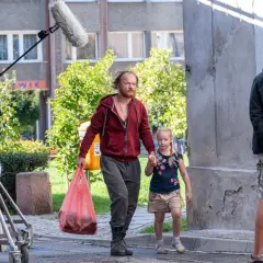 Mężczyzna z dziewczynką idą ulicą, za nimi ekipa filmowa z mikrofonem.