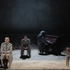 Trzy osoby siedzą na krzesłach. Jedna gra na pianinie, ubrana w kaptur. Jutro jest nasze.