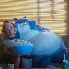 Wielki, niebieski kot przytula zmartwionego mężczyznę, który trzyma miskę popcornu. To scena z filmu "Jak pies z kotem", gdzie relacje między zwierzętami a ludźmi bywają skomplikowane.