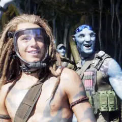 Jack Champion w masce i z dredami, obok uśmiechniętego Na'vi. W tle inni członkowie klanu.