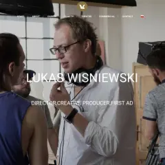 Łukasz Wiśniewski w białej koszuli z mikrofonem na szyi, na planie filmowym.