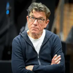 Mężczyzna w okularach, w granatowej bluzie, zastanawia się, ile zarabia aktor teatralny w Polsce.