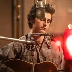 Młody muzyk z kompletnie nieznaną obsadą nagrywa piosenkę w studio, grając na gitarze i harmonijce ustnej.