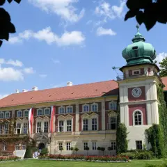 Pałac z zielonymi kopułami i zegarem, ozdobiony flagami, otoczony ogrodem.