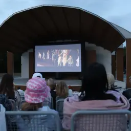 Wieczorne kino plenerowe na Białołęce. Widzowie oglądają film na dużym ekranie pod zadaszoną sceną.