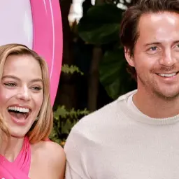Margot Robbie śmieje się obok Toma Ackerleya, który uśmiecha się do aparatu.