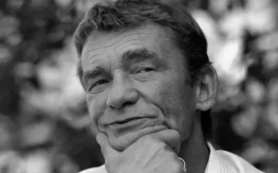 Portret Krzysztofa Kiersznowskiego z dłonią pod brodą, w tle rozmyte liście.