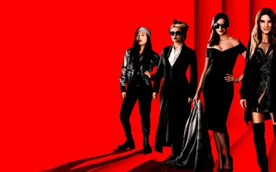Grupa eleganckich kobiet, gwiazd filmu Ocean's 8, pozuje na czerwonym tle.