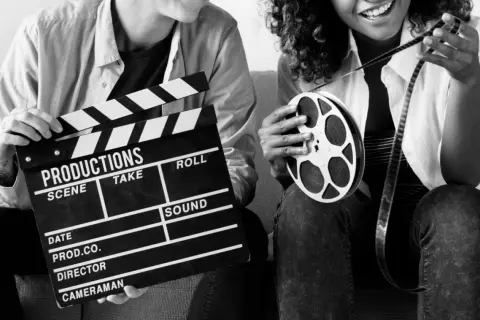Dwie osoby z klapsem filmowym i rolką taśmy filmowej. Zastanawiasz się, ile zarabia producent filmowy?