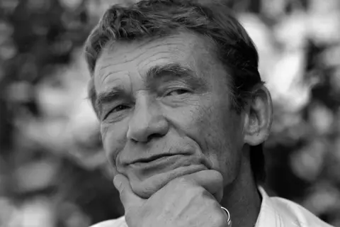 Portret Krzysztofa Kiersznowskiego z dłonią pod brodą, w tle rozmyte liście.