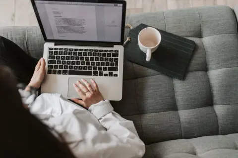 Kobieta pisze na laptopie, zastanawiając się, ile zarabia scenarzysta w Polsce. Obok kubek i tablet.