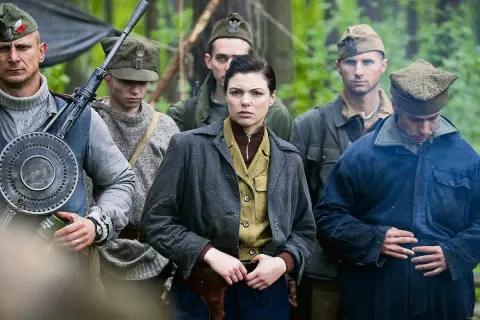 Grupa żołnierzy w lesie, w tym kobieta z pistoletem przy pasie. W tle widać broń maszynową. To scena z filmu "Czas honoru".
