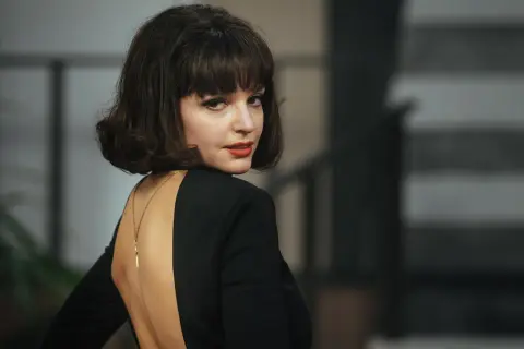 Elegancka Maria Dębska w czarnej sukni z głębokim wycięciem na plecach, zmysłowo odwraca głowę.