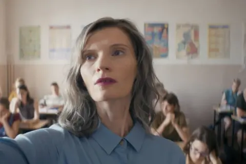 Nauczycielka w klasie, w tle widać innych ludzi, obsada filmu.