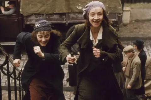 Dwie kobiety biegną po schodach, śmiejąc się radośnie. Jedna z nich trzyma butelkę wina. Bohaterka filmu niczego nie żałuje, ciesząc się chwilą.