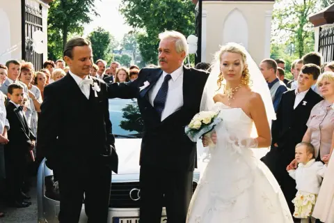Para młoda i goście na weselu Smarzowskim. Panna młoda w białej sukni, pan młody w garniturze.