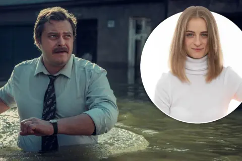 Mężczyzna w koszuli i krawacie brodzi w wodzie, obok uśmiechnięta kobieta w golfie. Wielka woda zalała miasto.