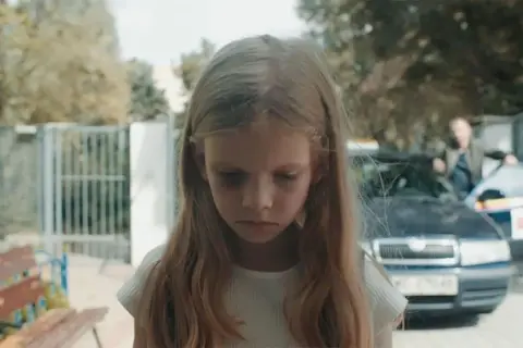 Smutna dziewczynka z sińcami pod oczami, w tle samochód i mężczyzna. Scena z filmu budząca konfuzję.
