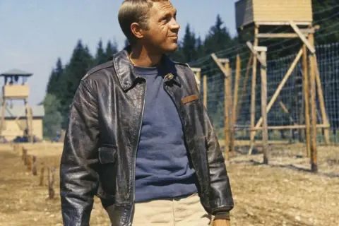 Steve McQueen w skórzanej kurtce, w tle obóz jeniecki.