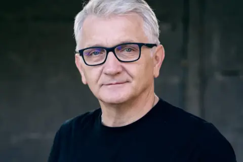 Portret Dariusza Kowalskiego, aktora, w okularach i czarnej koszulce.