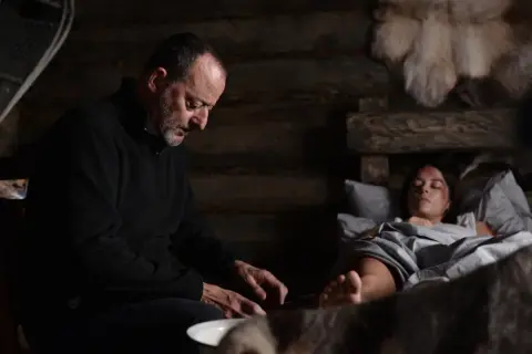 Jean Reno w "Cold Blood Legacy" obsada: mężczyzna pochyla się nad ranną kobietą w chatce.