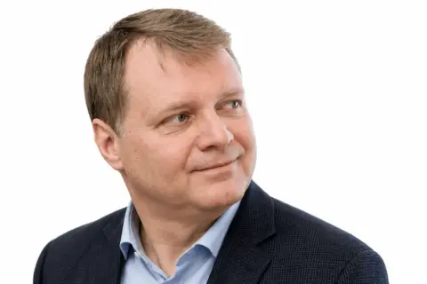 Uśmiechnięty Jacek Sobala w granatowej marynarce i błękitnej koszuli, patrzący w bok.