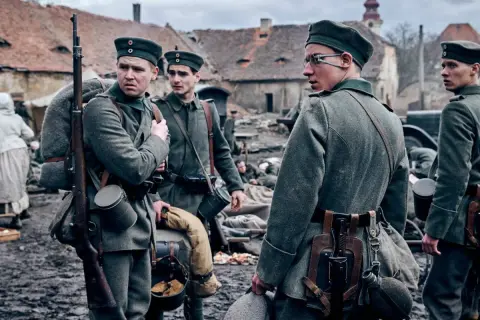 Żołnierze w mundurach z I wojny światowej, z karabinami i plecakami, stoją na błotnistym podwórzu. Na zachodzie bez zmian obsada.