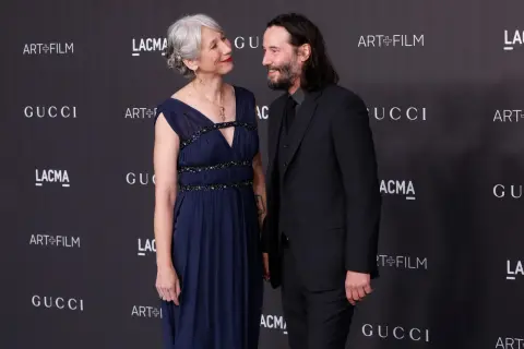 Alexandra Grant wzrost jest widoczny obok Keanu Reevesa. Oboje pozują na tle logo Gucci i Art+Film.