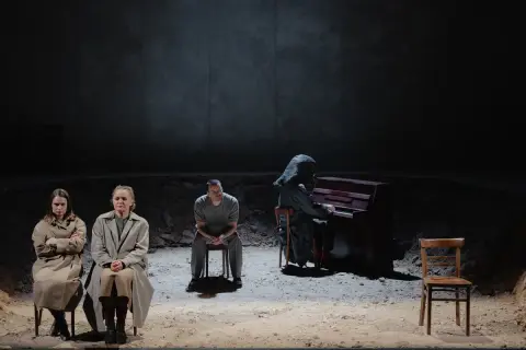 Trzy osoby siedzą na krzesłach. Jedna gra na pianinie, ubrana w kaptur. Jutro jest nasze.
