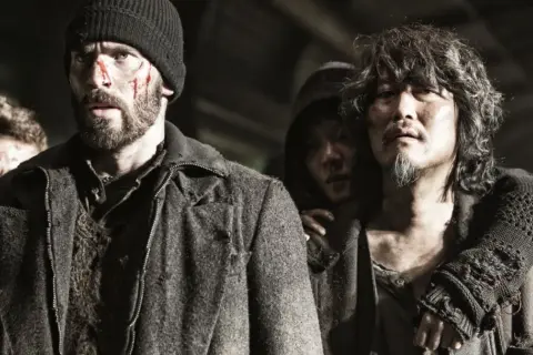 Zraniona obsada Snowpiercer: Arka przyszłości, w tym Chris Evans, w surowych, postapokaliptycznych strojach.