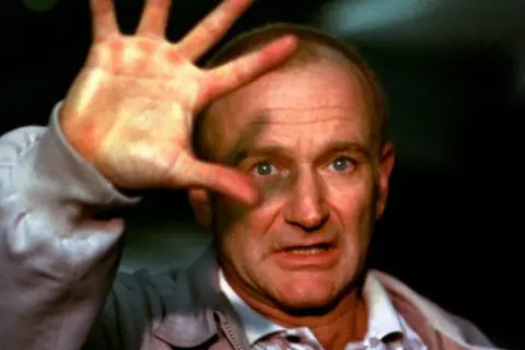 Robin Williams, który zdobył Oscara za rolę w "Buntowniku z wyboru", z dłonią przed twarzą.