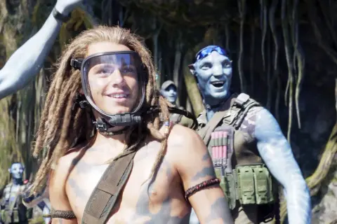 Jack Champion w masce i z dredami, obok uśmiechniętego Na'vi. W tle inni członkowie klanu.
