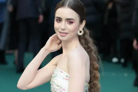 Lily Collins, gwiazda serialu "Emily w Paryżu", w kwiecistej sukni i z błyszczącymi kolczykami.