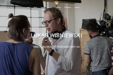 Łukasz Wiśniewski w białej koszuli z mikrofonem na szyi, na planie filmowym.