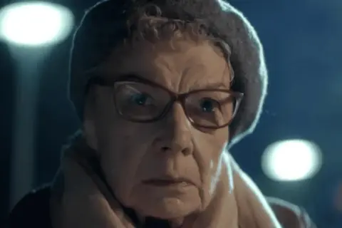 Aleksandra Górska w okularach i czapce, zamyślona, w świetle latarni.