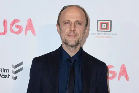 Łukasz Simlat, znany z wielu polskich filmów, na tle napisu "JUGA" i logo Polskiego Instytutu Sztuki Filmowej.